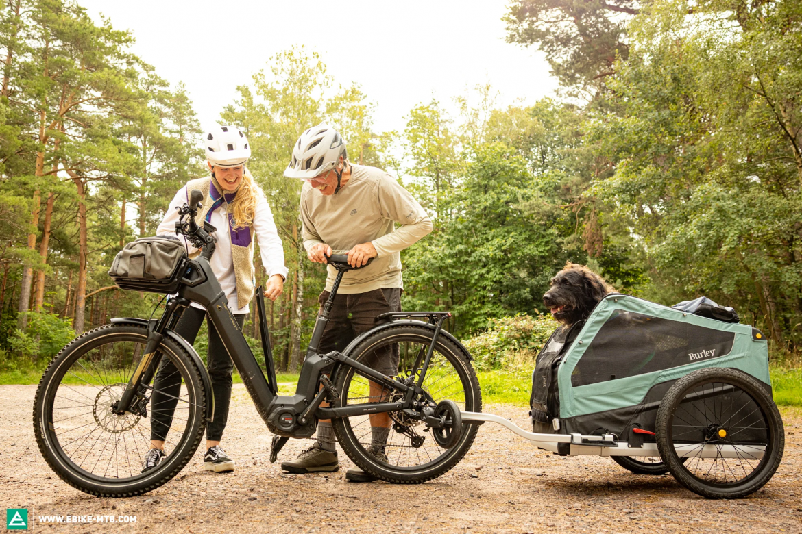 Couple using an electric bike with a cargo trailer for camping, transporting gear and pets in an outdoor forest environment, highlighting e-bike versatility for camping logistics.